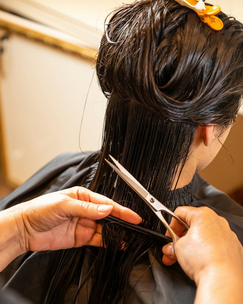Long dark hair being cut straight across with scissors